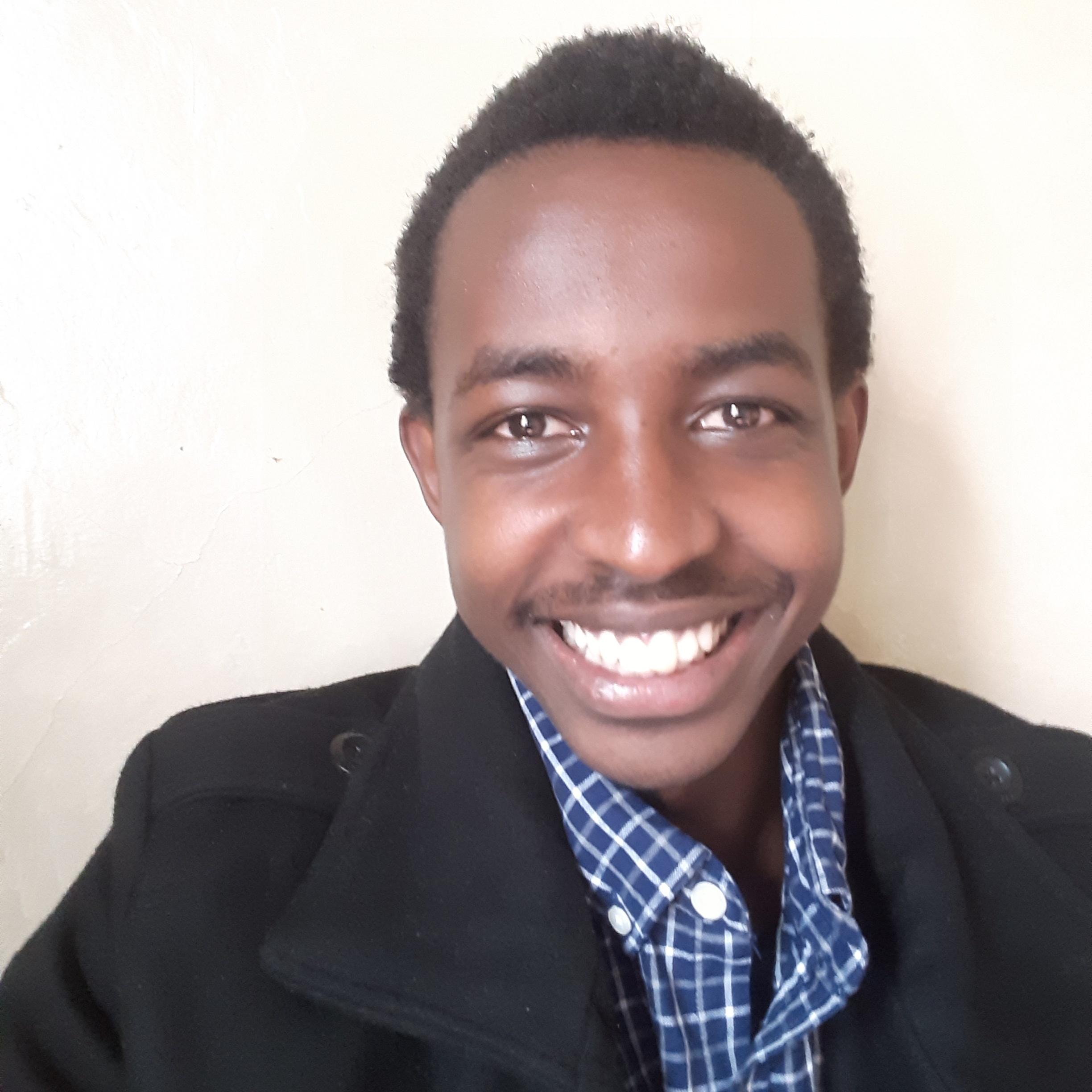 An image of Brian Mwangi in a black coat and blue striped shirt smiling